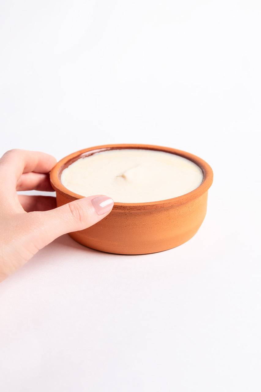 Hand holding a terracotta bowl with solid dishwashing soap on a white background