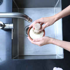 Person washing a pot under running water in a kitchen sink.