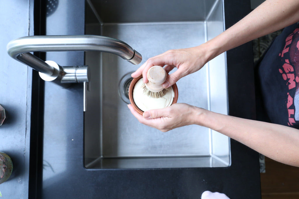 Person washing a pot under running water in a kitchen sink.