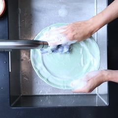 Person washing a green plate in a sink with soap and water.