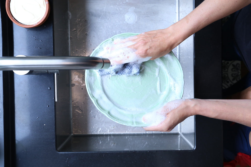 Person washing a green plate in a sink with soap and water.